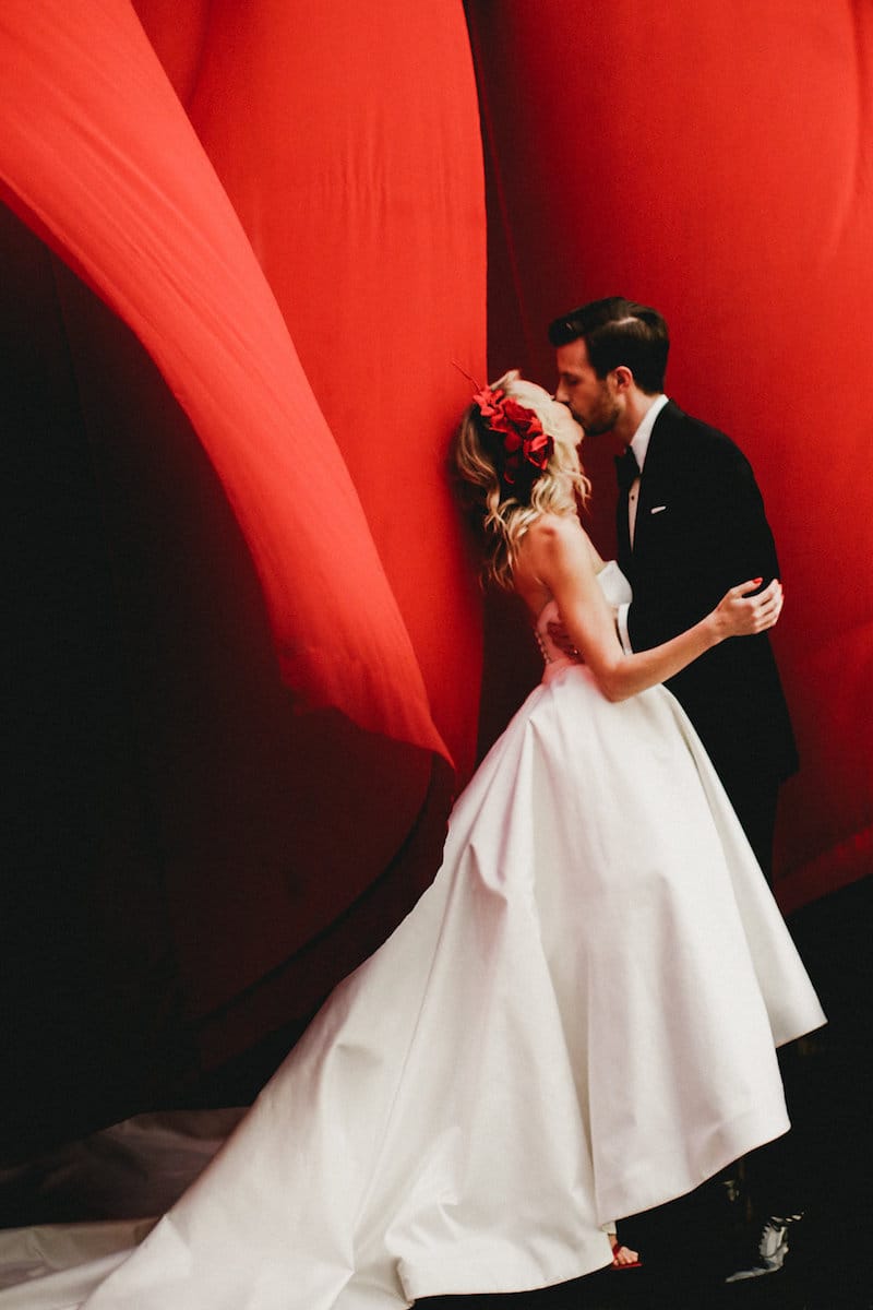 bride and groom in front of red background